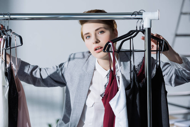 stylish woman standing between clothes hanging on rack - Fotografie, Obrázek