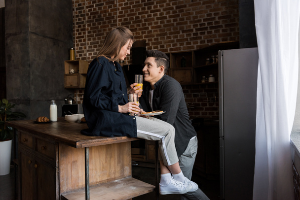 smiling couple with orange juice looking at each other at kitchen - Photo, Image