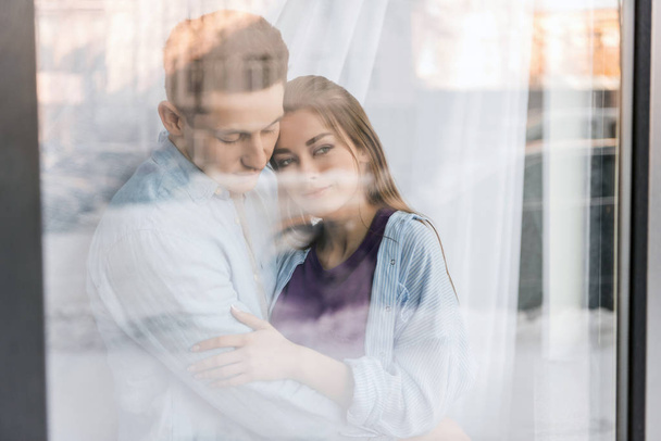 view through window on couple hugging and looking away - Zdjęcie, obraz