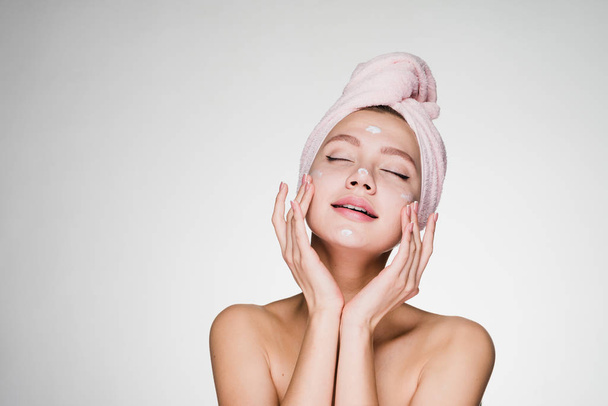 woman with a towel on her head puts cream on her face - Fotoğraf, Görsel