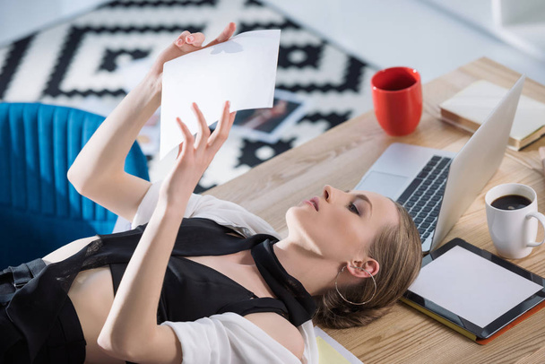 attractive fashion designer lying on desk and looking at sketch - Photo, Image
