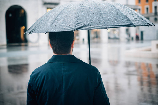 Rainy day in the city and businessman holding umbrella - Zdjęcie, obraz