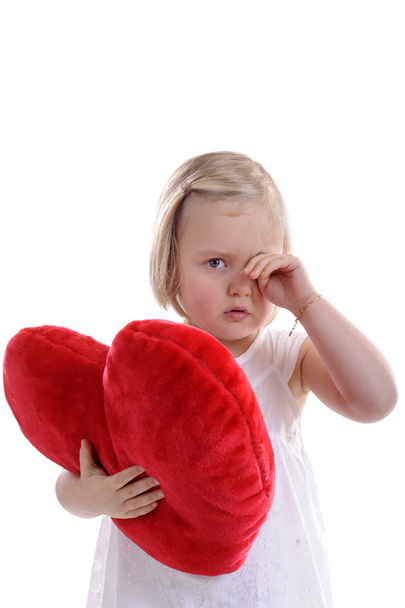 Petite fille fatiguée avec un oreiller rouge en forme de coeur frottant ses yeux
 - Photo, image