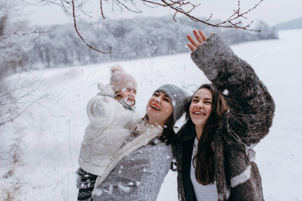Madre sosteniendo a su hija más pequeña en las manos y divirtiéndose juntos en el parque de invierno
 - Foto, Imagen