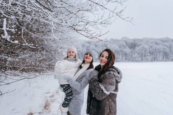 Mutter hält kleinere Tochter in den Händen und vergnügt sich gemeinsam im Winterpark - Foto, Bild