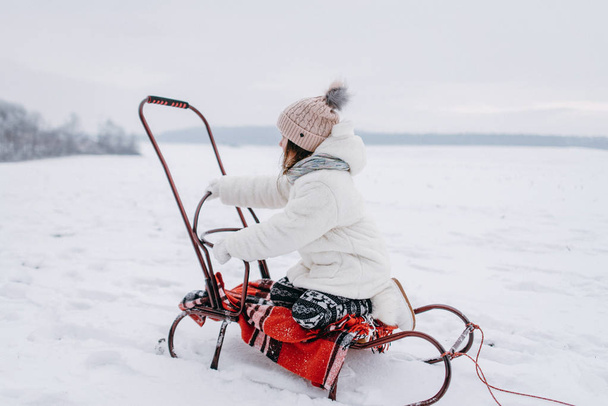 Μικρό κορίτσι ανάπαυσης σε έλκηθρο με καρώ κουβέρτα στο χειμερινό πάρκο - Φωτογραφία, εικόνα