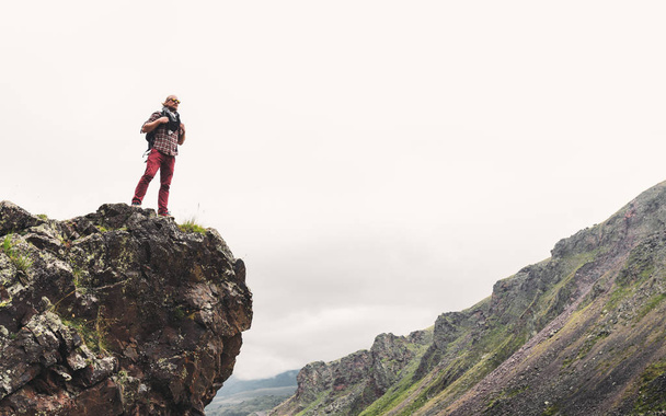 Young Man With Backpack Standing On Rocky Stone In Summer Mountains And Looking Into The Distance. Wanderlust Travel Journey Concept - Foto, afbeelding