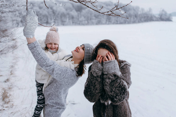 Madre sosteniendo a su hija más pequeña en las manos y divirtiéndose juntos en invierno
 - Foto, imagen