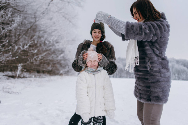 Madre divirtiéndose y bromeando con las hijas en el parque de invierno
  - Foto, imagen