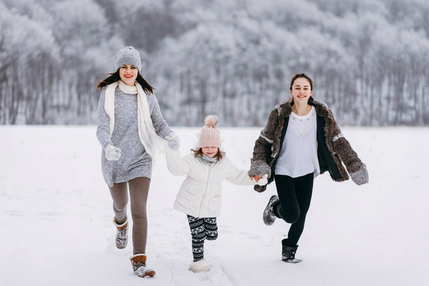 Etunäkymä perheen käynnissä lumella talvipuiston taustalla
 - Valokuva, kuva