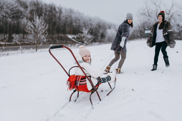 Мать со старшей дочерью катается на санках с младшей дочерью в зимнем парке
 - Фото, изображение