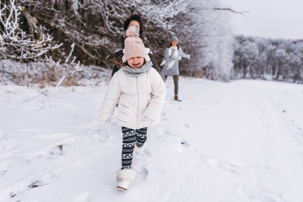Madre con hijas corriendo y divirtiéndose afuera en invierno
 - Foto, Imagen