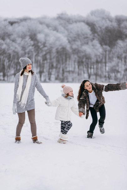 Sivukuva perheen käynnissä lunta talvipuiston taustalla
 - Valokuva, kuva