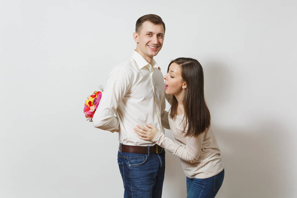 Couple in love. Woman looking behind man who hiding behind him bouquet of beautiful roses flowers isolated on white background. St. Valentine's Day, International Women's Day birthday holiday concept - Valokuva, kuva