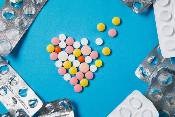 Leki kolorowe okrągłe tabletki w postaci dyfuzji serca na białym tle na niebieskim tle. Puste opakowania wokół kształtu pigułki. Koncepcja zdrowia leczenie wybór zdrowego stylu życia. Kopiować miejsca ogłoszenie - Zdjęcie, obraz