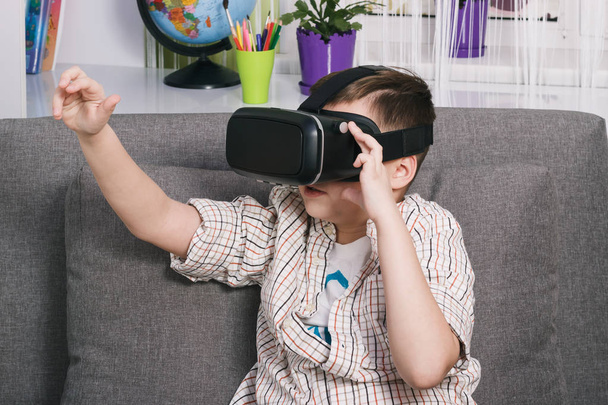 Niño juega con gafas de realidad virtual, en el interior. Dispositivo de realidad virtual digital
 - Foto, Imagen