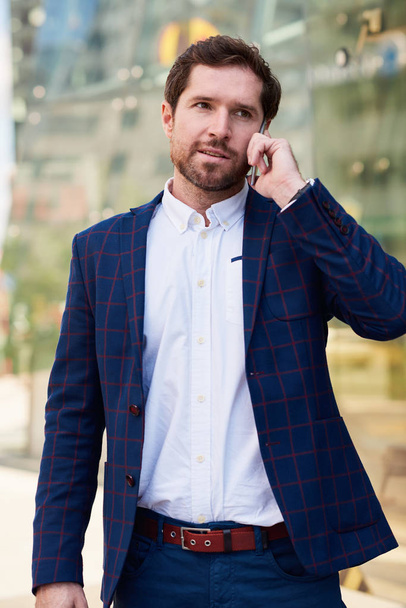 Успішний молодий бізнесмен у костюмі розмовляє на мобільному телефоні під час прогулянки по місту
 - Фото, зображення