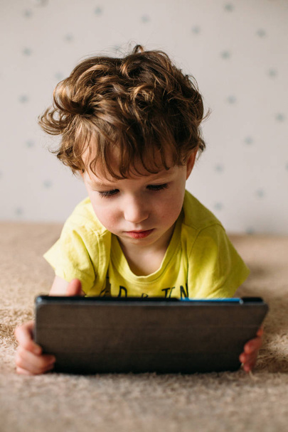 Cute little boy using a pad. Child playing with digital tablet lying on a bed. Free time. Tehnology and internet concept - Photo, image