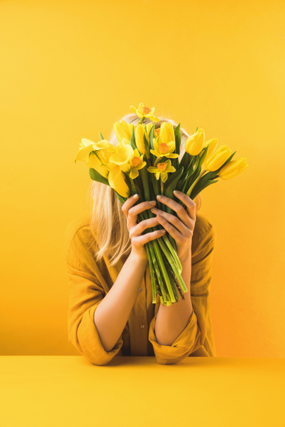 young woman holding beautiful yellow tulips and daffodils on yellow - Photo, Image