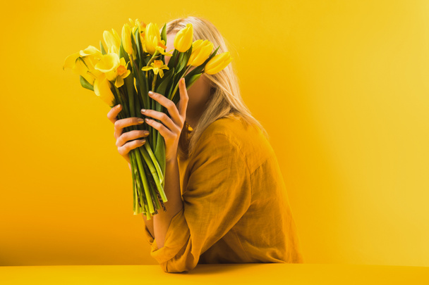 junge Frau mit schönen gelben Frühlingsblumen auf gelbem Grund  - Foto, Bild