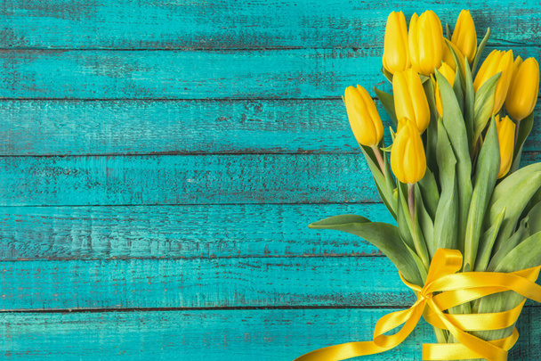 beautiful yellow tulips with ribbon on turquoise wooden surface  - Photo, Image