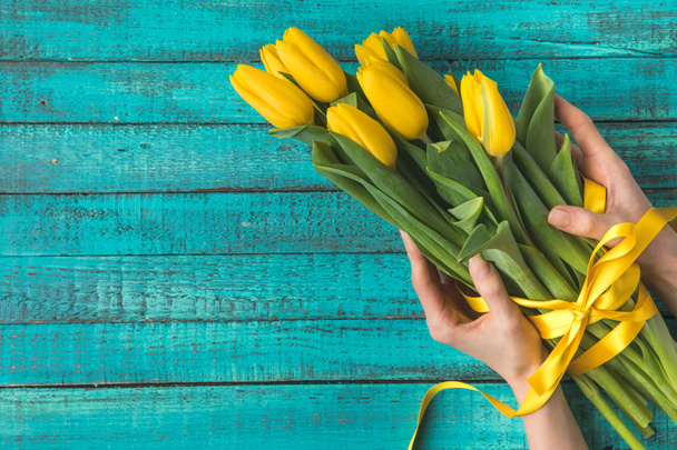 vista superior das mãos segurando belas tulipas amarelas com fita
  - Foto, Imagem