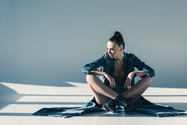 chica atractiva en ropa de mezclilla sentado en el suelo con sombras
 - Foto, Imagen