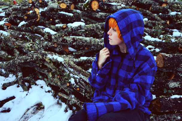 雪ログ背景に屋外青冬ジャケットのポーズで赤毛の若い女性 - 写真・画像
