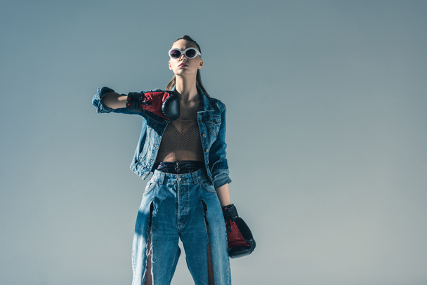 beautiful stylish girl in denim and sunglasses posing with boxing gloves, isolated on grey - Fotoğraf, Görsel