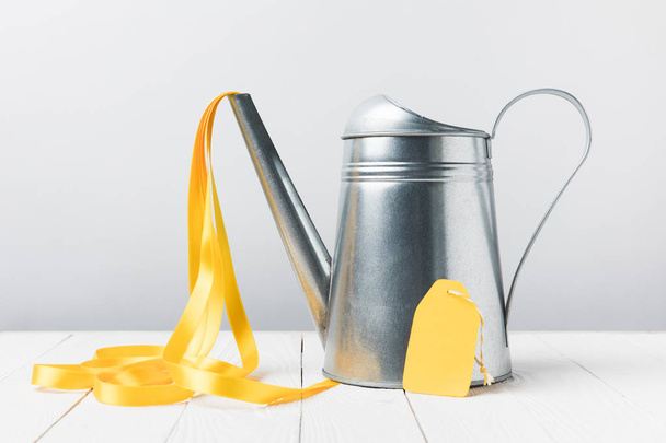 close-up view of shiny watering can with yellow ribbon and blank label on grey - Фото, зображення