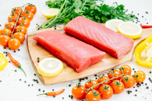 Carne de filete de atún crudo en tabla de cortar de madera con verduras e ingredientes para cocinar
 - Foto, Imagen