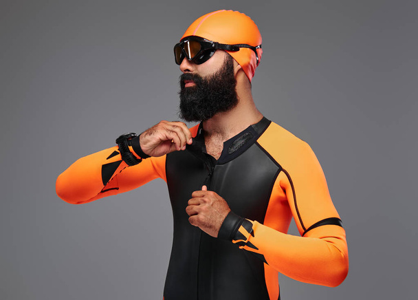 Parrakkaan miehen muotokuva oranssissa neopreenisukelluspuvussa ja harmaalla pohjalla eristetty sukellusnaamio
. - Valokuva, kuva