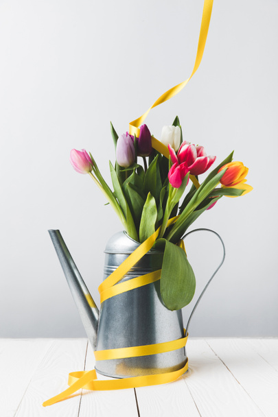 beautiful blooming tulip flowers in watering can with yellow ribbon on grey - Foto, imagen