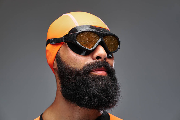 Retrato de close-up de um macho barbudo em terno de neoprene laranja e máscara de mergulho isolado em fundo cinza
. - Foto, Imagem