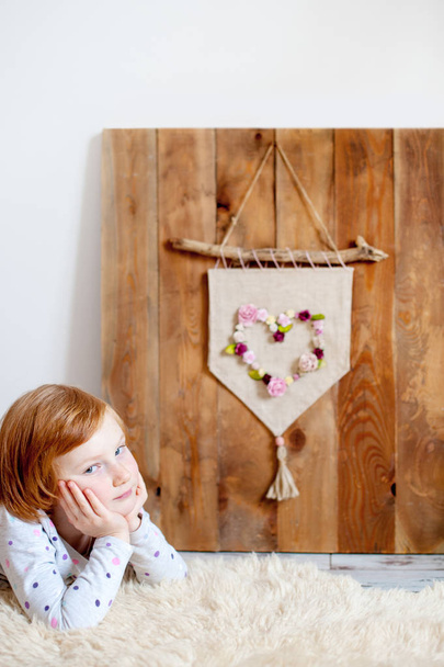 Redheaded girl heals on sheepskin in front of background with a pennant - Фото, изображение