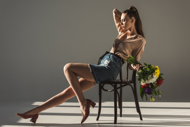 fashionable elegant girl with bouquet of flowers posing on chair - Fotó, kép