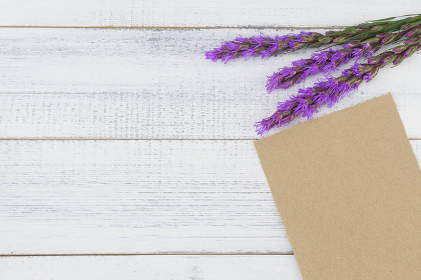 Blank brown card decorated with violet liatris flowers on white wood background with copy space - Foto, afbeelding