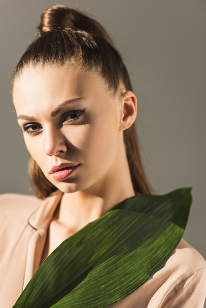 beautiful brunette girl with green leaf, isolated on grey - Zdjęcie, obraz