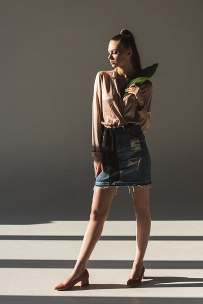 stylish woman in denim skirt and blouse holding green leaf - Photo, image