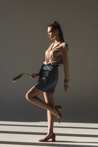 fashionable young woman in denim skirt and blouse holding green leaf - Photo, Image