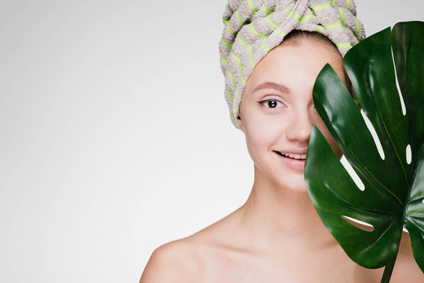 happy woman with a towel on her head after a shower holds a big leaf in her hands - Foto, Imagen