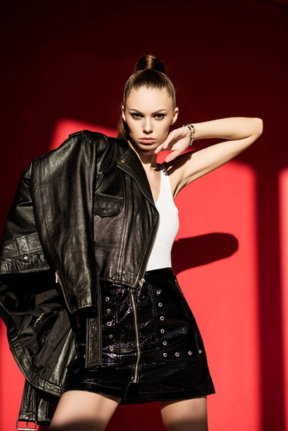 stylish caucasian girl posing in black leather jacket for fashion shoot on red - Fotó, kép
