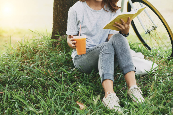 Imagen recortada de una estudiante bebiendo cóctel y leyendo un libro en el parque
 - Foto, imagen