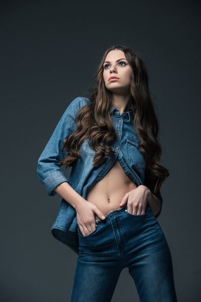 girl with long hair posing in trendy denim clothes, isolated on grey - 写真・画像