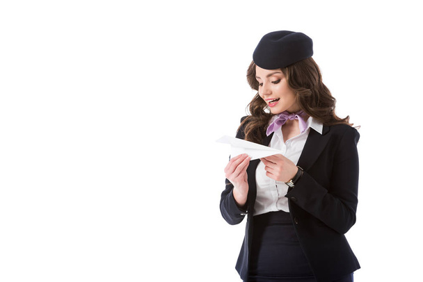 attractive stewardess looking at paper plane isolated on white - Foto, Bild