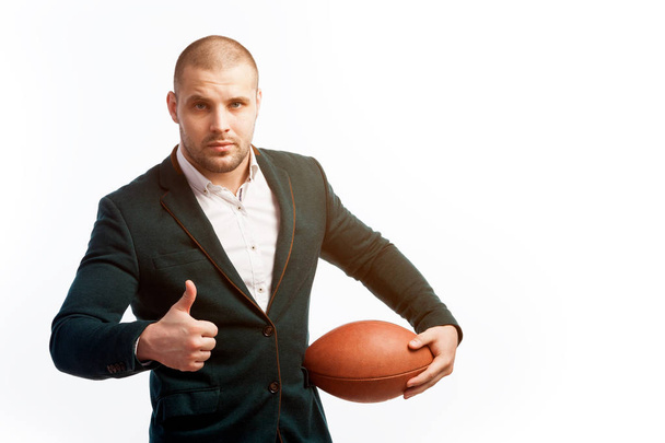 A young bald man in a white shirt, green suit holds a rugby ball poses on a white isolated background - Foto, Imagem