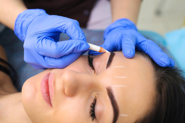 Young beautiful woman making permanent makeup in cosmetology salon. - 写真・画像