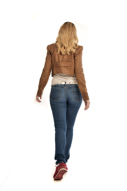 retrato de longitud completa de chica rubia con chaqueta marrón y jeans. pose de pie sobre fondo blanco
. - Foto, Imagen