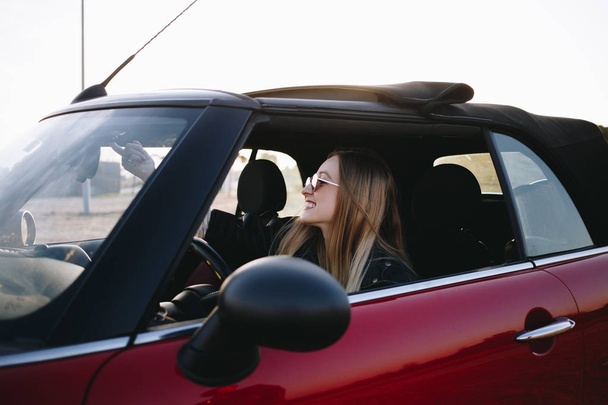 portrait of young woman sitting in car at sunset - Foto, imagen