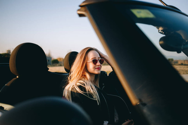 πορτρέτο του νεαρή γυναίκα που κάθεται στο αυτοκίνητο στο ηλιοβασίλεμα - Φωτογραφία, εικόνα